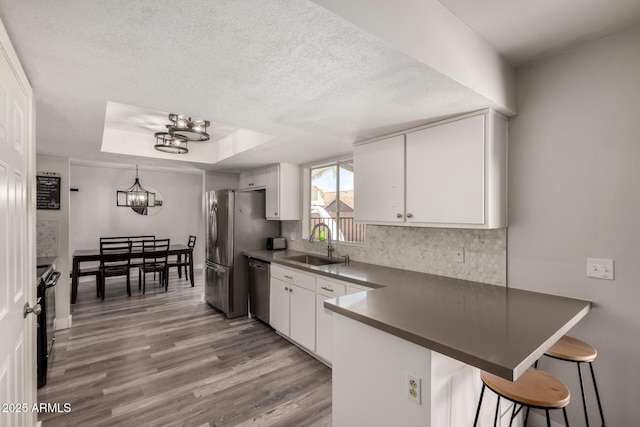 kitchen featuring a peninsula, white cabinets, tasteful backsplash, a sink, and appliances with stainless steel finishes