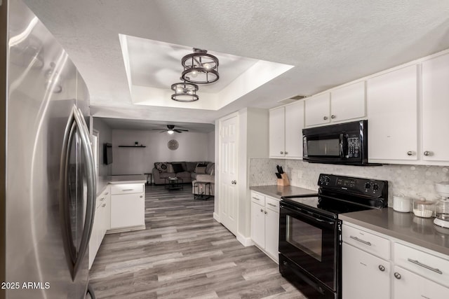 kitchen featuring open floor plan, light wood-type flooring, a raised ceiling, white cabinets, and black appliances