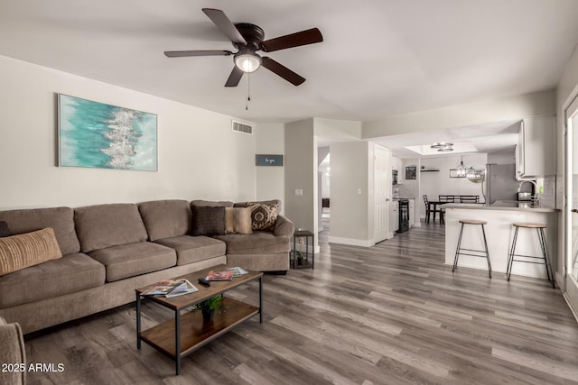 living room with baseboards, visible vents, wood finished floors, and ceiling fan with notable chandelier