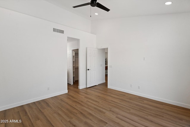 unfurnished bedroom with baseboards, wood finished floors, recessed lighting, a walk in closet, and a high ceiling