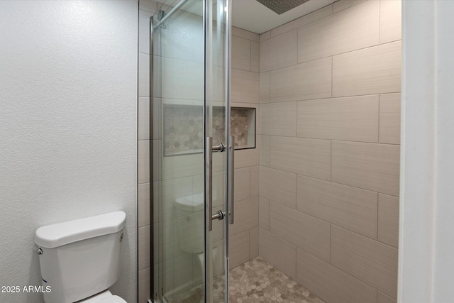 bathroom with toilet, a shower stall, and a textured wall