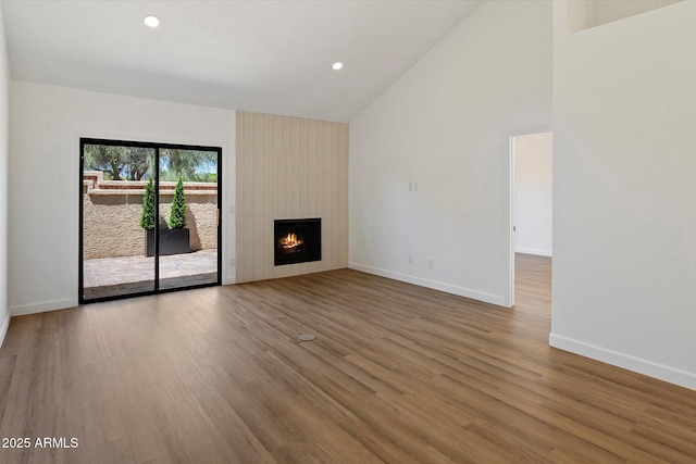 unfurnished living room featuring wood finished floors, baseboards, a fireplace, recessed lighting, and high vaulted ceiling