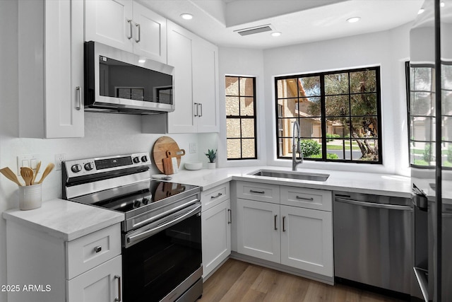 kitchen with stainless steel appliances, a sink, plenty of natural light, white cabinets, and recessed lighting