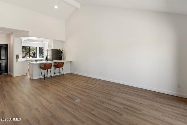 living room with wood finished floors, beam ceiling, baseboards, high vaulted ceiling, and recessed lighting