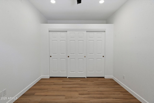 unfurnished bedroom with baseboards, wood finished floors, recessed lighting, and a closet