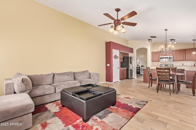 living room featuring arched walkways, ceiling fan with notable chandelier, light wood-type flooring, and lofted ceiling