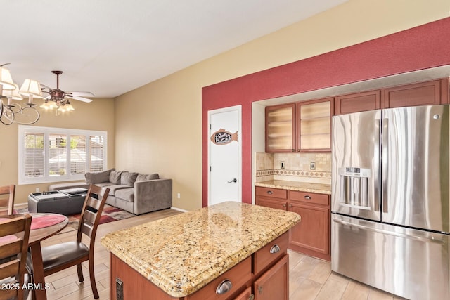 kitchen with brown cabinets, light stone counters, backsplash, stainless steel refrigerator with ice dispenser, and glass insert cabinets