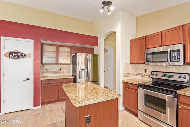 kitchen with a kitchen island, light stone countertops, tasteful backsplash, arched walkways, and appliances with stainless steel finishes