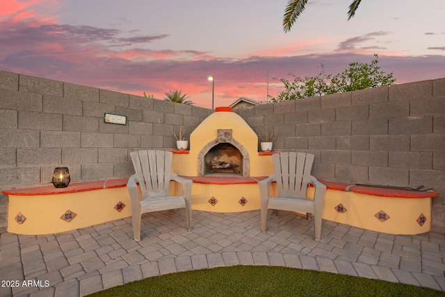 patio terrace at dusk with an outdoor fireplace and fence