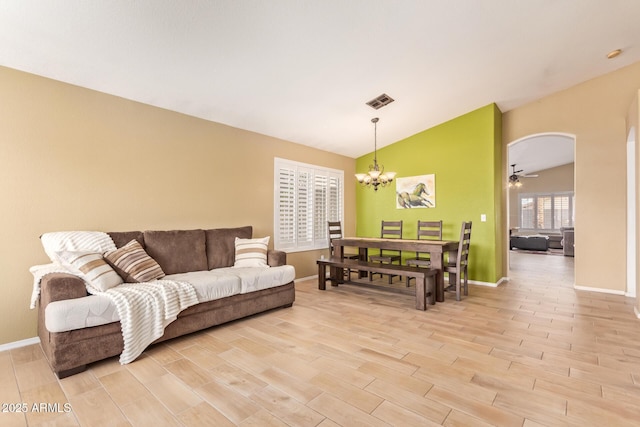 living room featuring visible vents, baseboards, light wood finished floors, a notable chandelier, and lofted ceiling