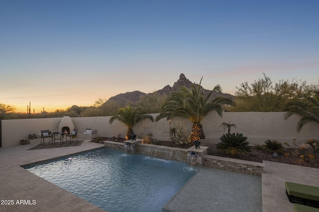 pool at dusk featuring pool water feature and a patio area