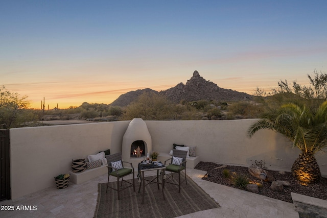 patio terrace at dusk with exterior fireplace and a mountain view