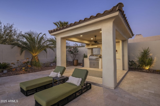 patio terrace at dusk featuring ceiling fan, an outdoor kitchen, and area for grilling