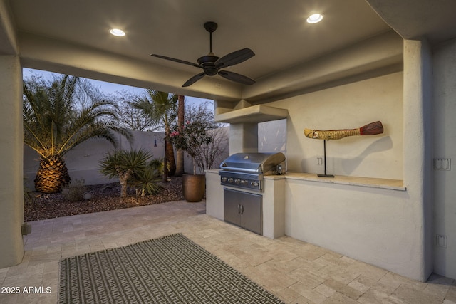 patio terrace at dusk with ceiling fan, area for grilling, and exterior kitchen