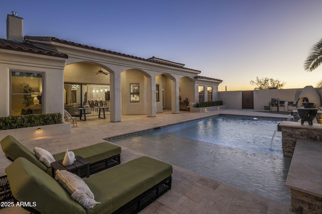 pool at dusk featuring ceiling fan, pool water feature, and a patio area