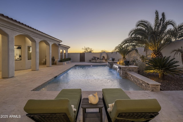 pool at dusk with pool water feature and a patio