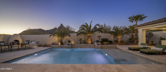 pool at dusk with pool water feature and a patio area