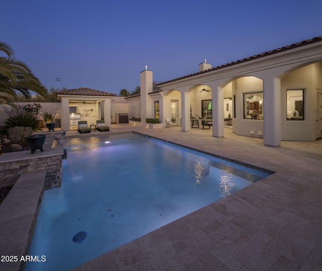 pool at dusk featuring ceiling fan and a patio