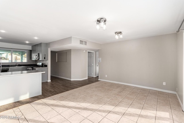 kitchen with gray cabinetry, sink, light tile patterned floors, and stove