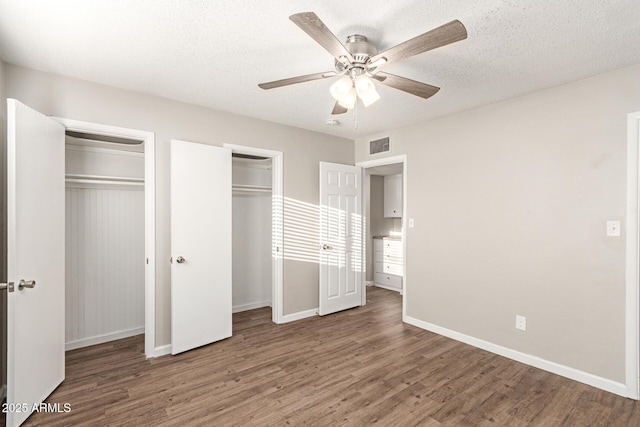 unfurnished bedroom with ceiling fan, two closets, a textured ceiling, and dark hardwood / wood-style flooring