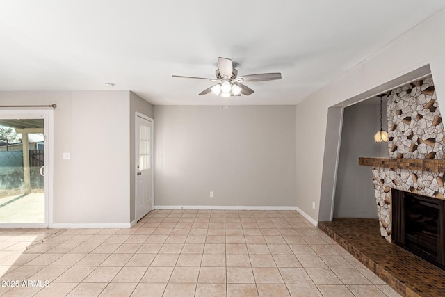 spare room with ceiling fan, a stone fireplace, and light tile patterned floors