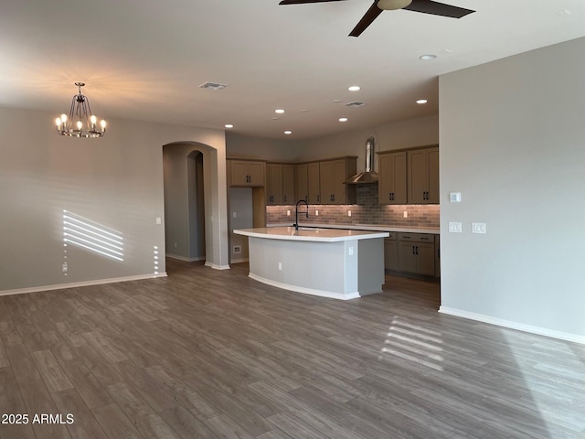 kitchen with decorative light fixtures, sink, backsplash, a center island with sink, and wall chimney exhaust hood