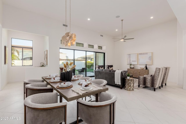 tiled dining space with ceiling fan, a healthy amount of sunlight, and a high ceiling