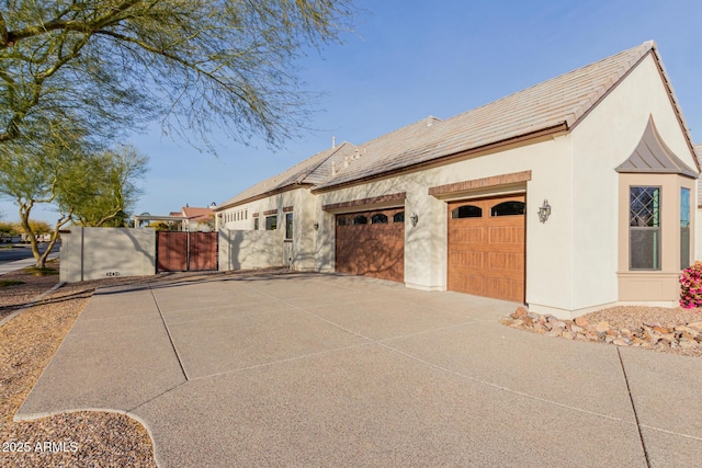 view of property exterior with stucco siding, driveway, a garage, and a gate