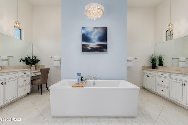 full bath featuring a freestanding tub, marble finish floor, vanity, and an inviting chandelier