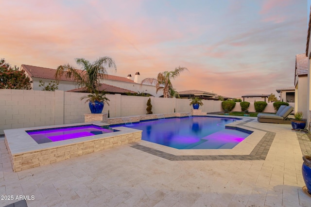 pool at dusk featuring a patio area and an in ground hot tub