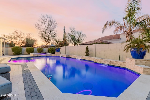 pool at dusk featuring pool water feature and an in ground hot tub