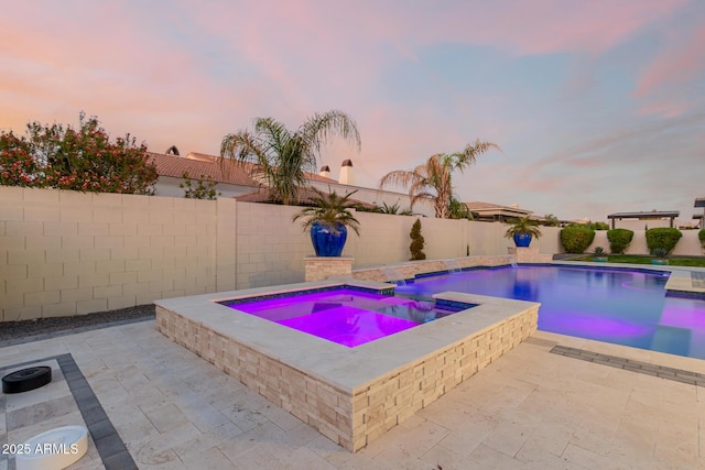 pool at dusk with a patio and an in ground hot tub