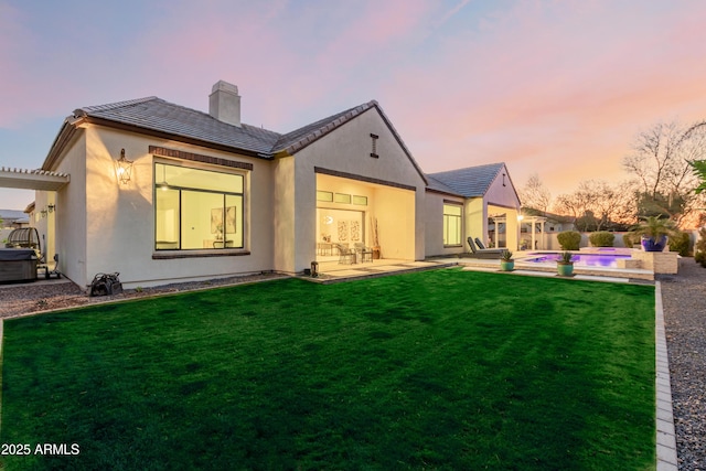 back house at dusk featuring a swimming pool with hot tub, a pergola, a patio, and a lawn