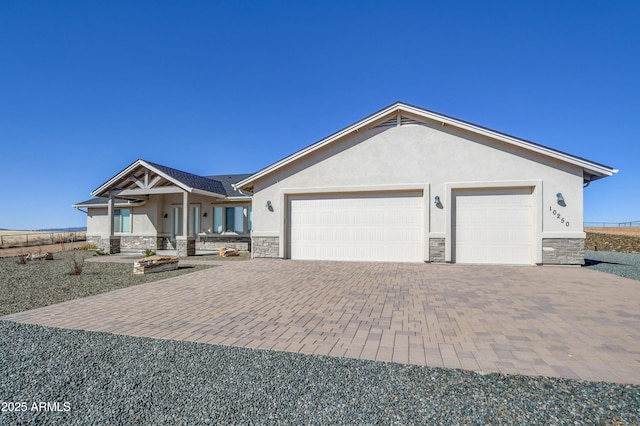 view of front of house with decorative driveway, stone siding, an attached garage, and stucco siding