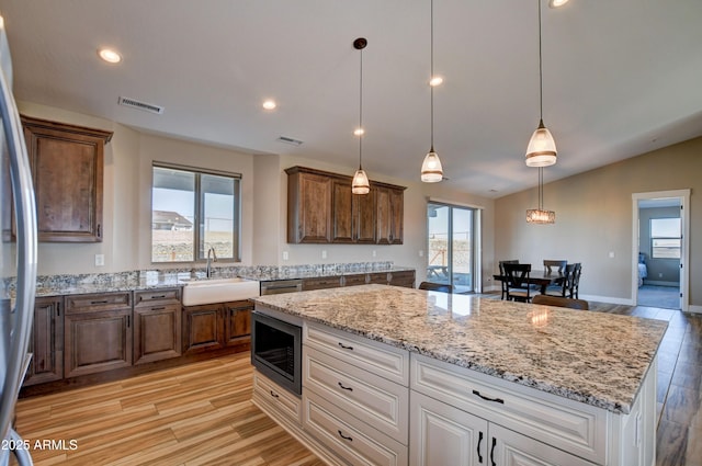 kitchen featuring light stone counters, visible vents, light wood-style flooring, a sink, and stainless steel appliances