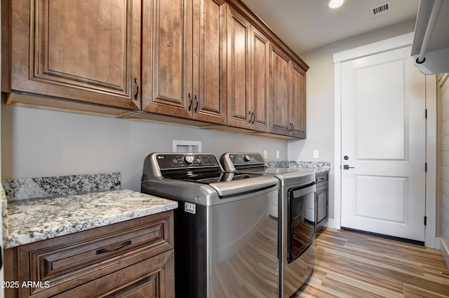 washroom with light wood-style floors, cabinet space, visible vents, and washing machine and clothes dryer