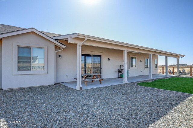 rear view of house with a patio area, stucco siding, a yard, and fence