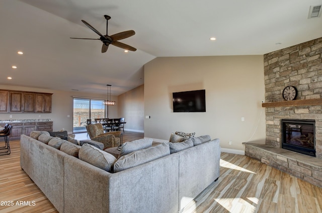 living room with a stone fireplace, vaulted ceiling, and light wood-type flooring