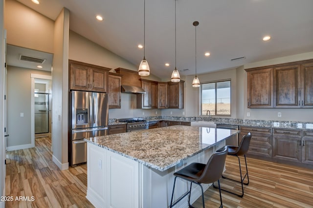 kitchen with visible vents, a center island, stainless steel appliances, wall chimney exhaust hood, and a sink