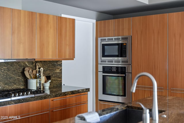 kitchen featuring range hood, sink, dark stone countertops, backsplash, and stainless steel appliances