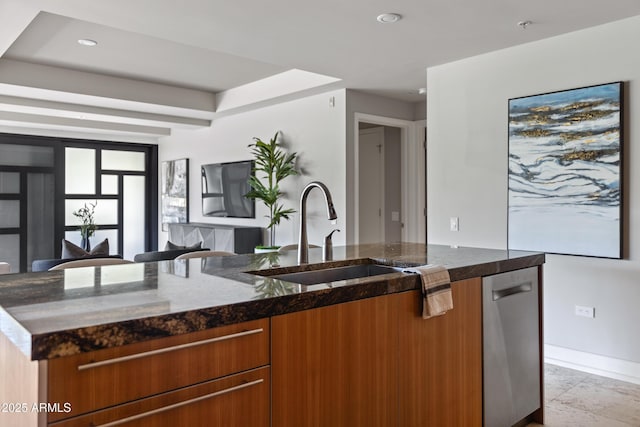 kitchen featuring stainless steel dishwasher, a kitchen island with sink, sink, and dark stone counters