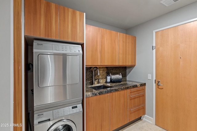 washroom featuring sink, cabinets, and stacked washing maching and dryer