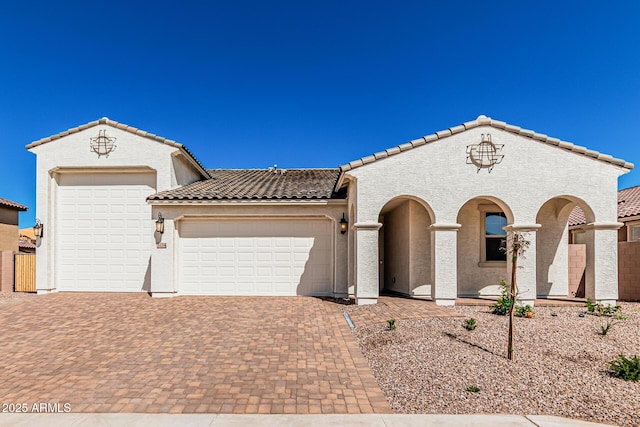 mediterranean / spanish home featuring a tiled roof, decorative driveway, a garage, and stucco siding