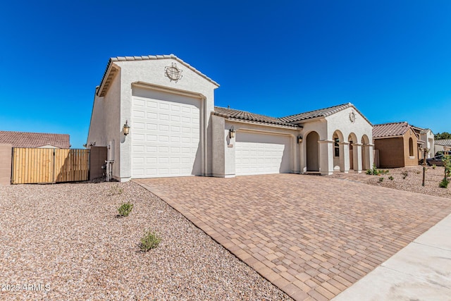 mediterranean / spanish house with a tile roof, decorative driveway, an attached garage, and stucco siding