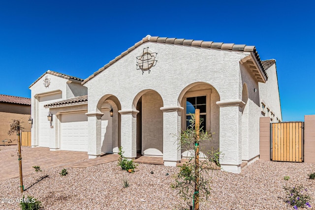 mediterranean / spanish-style house with stucco siding, driveway, a gate, an attached garage, and a tiled roof