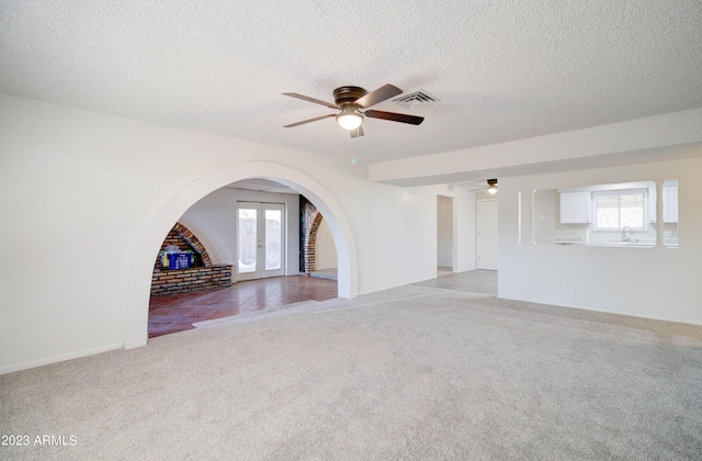 unfurnished living room with a wealth of natural light, light colored carpet, french doors, and a textured ceiling