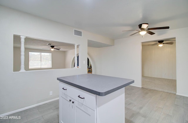 kitchen with ornate columns, a center island, white cabinets, and light hardwood / wood-style flooring