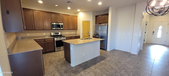 kitchen with decorative backsplash, appliances with stainless steel finishes, a kitchen island with sink, sink, and a chandelier