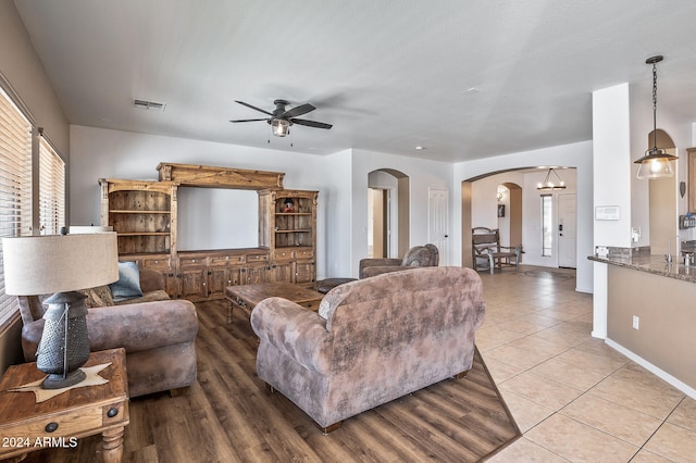 tiled living room with ceiling fan with notable chandelier