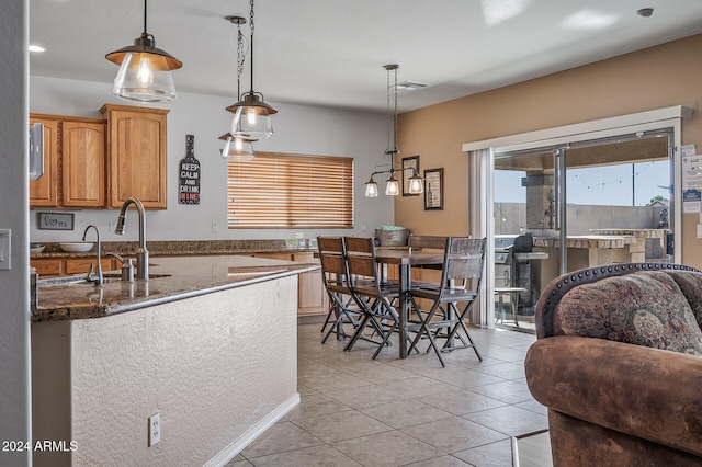 kitchen featuring sink, light tile patterned flooring, hanging light fixtures, and dark stone countertops